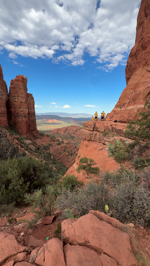 Hikers standing on a red rock ledge above the Sedona valley
