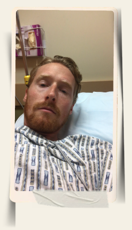 Nate lying in a hospital bed wearing a patterned gown