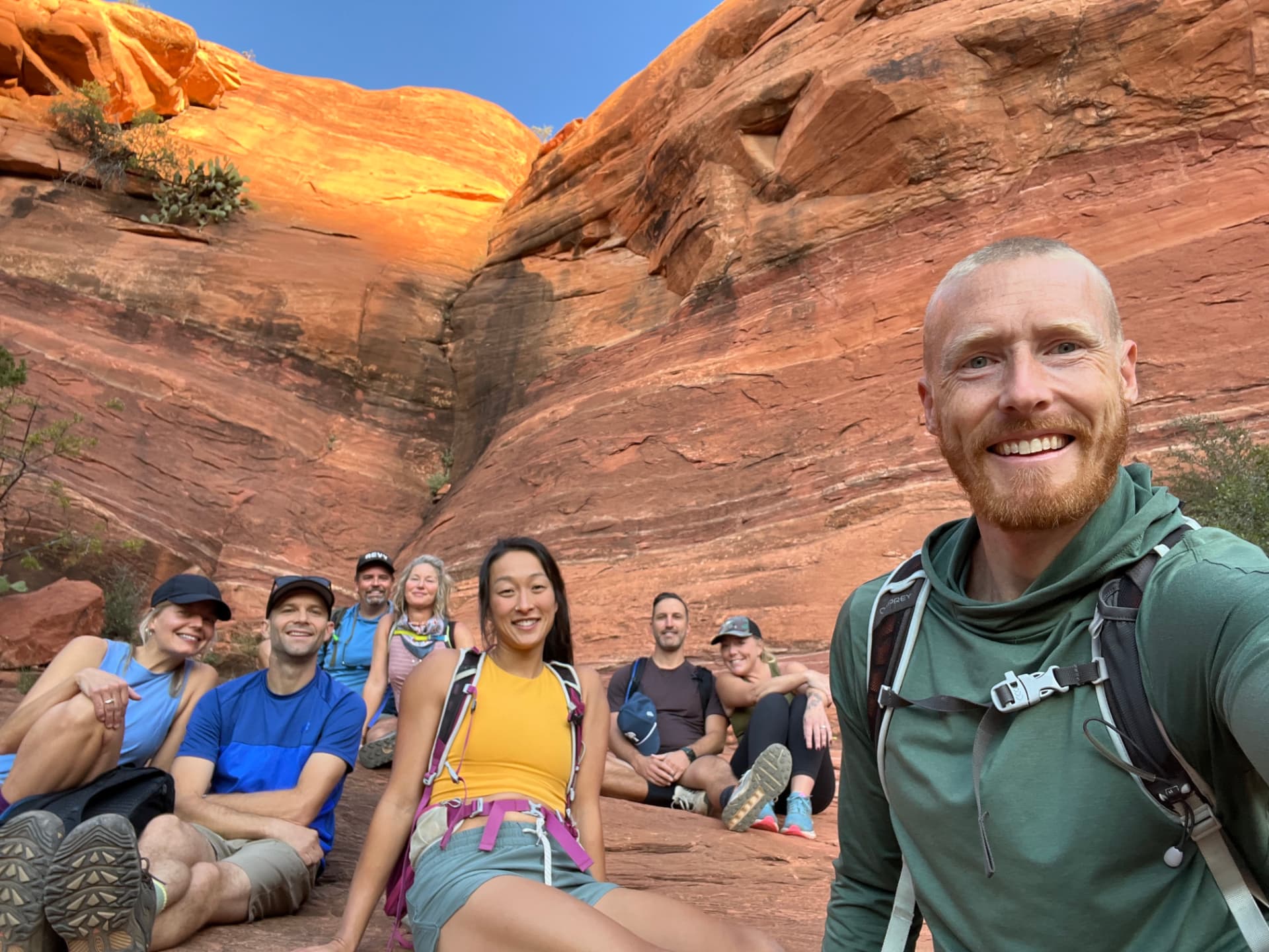 The group gathered and smiling on warm red rock after the climb