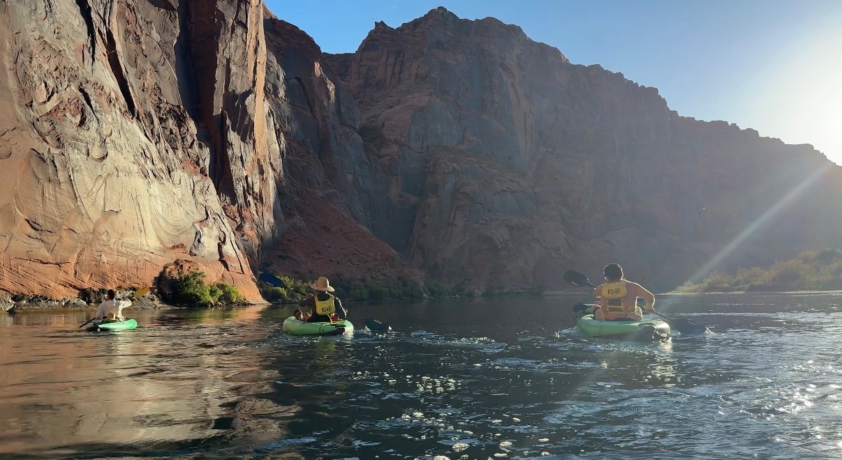 Three kayakers paddling beneath red canyon walls at golden hour