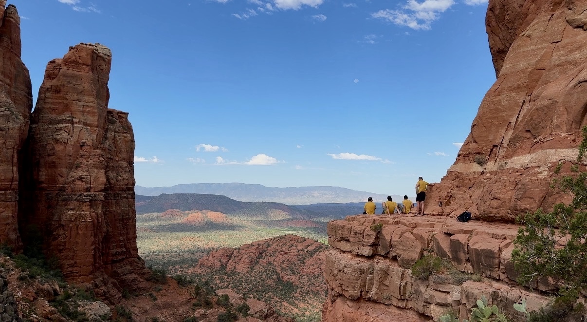 Hikers resting on a red rock ledge high above the Sedona valley