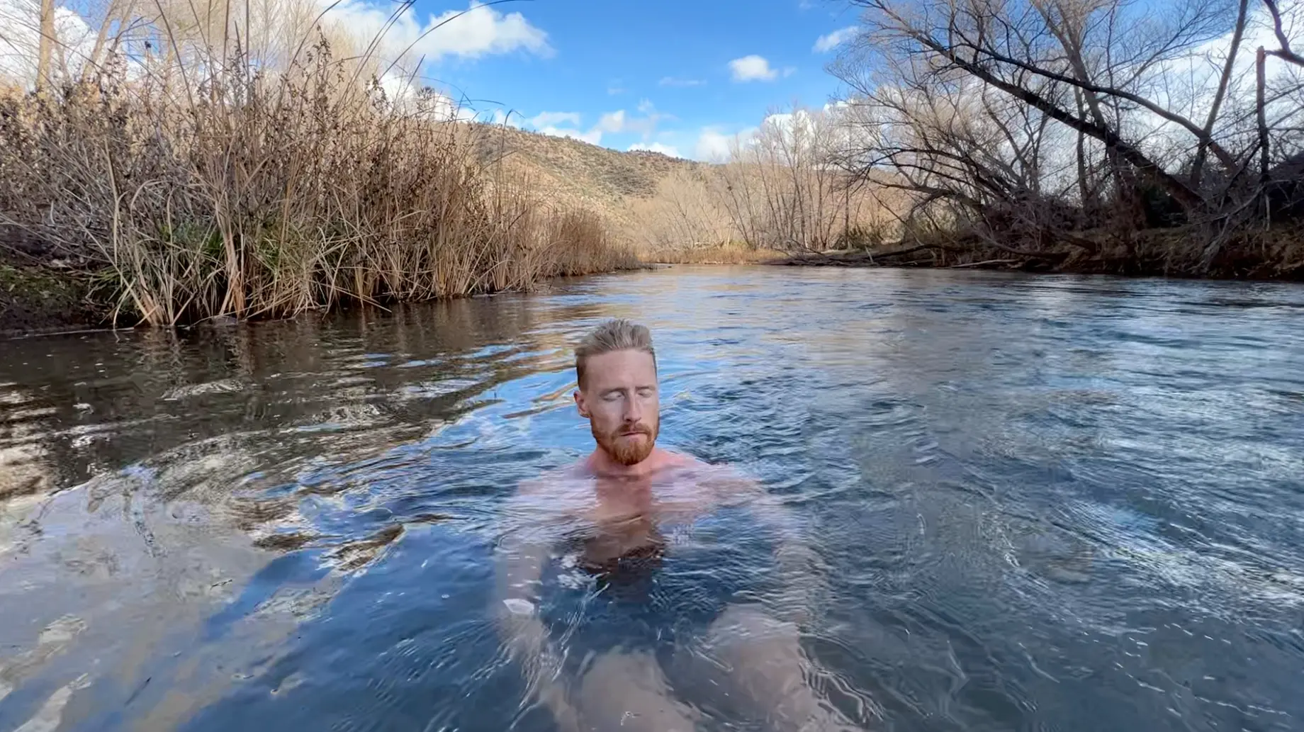Nate submerged in a river surrounded by winter trees and Sedona hills