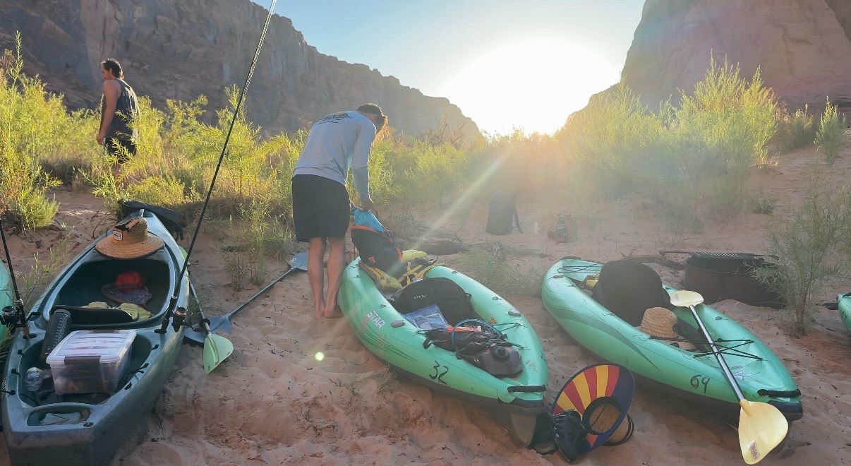 Kayaks packed on a sandy beach as the sun rises over the canyon